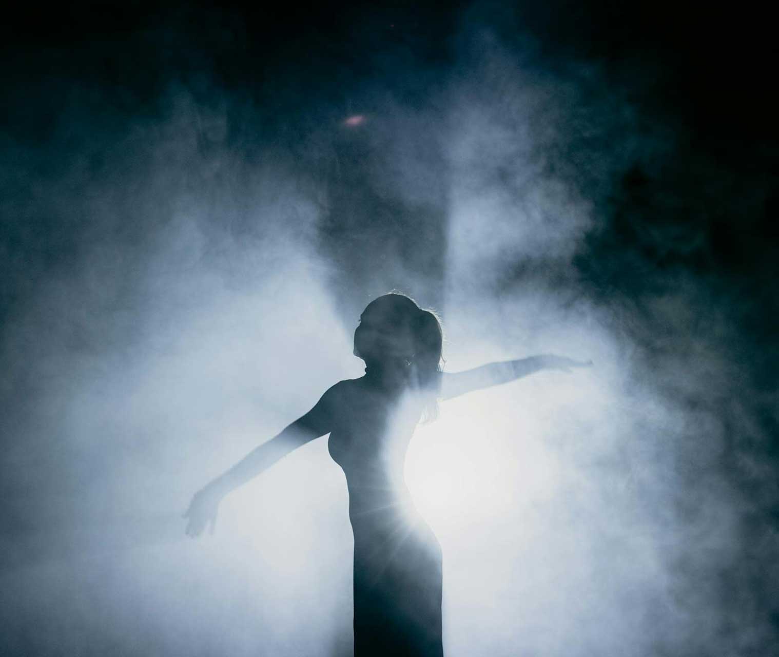 Femme dansant sur scène à contre-jour, entourée de fumée